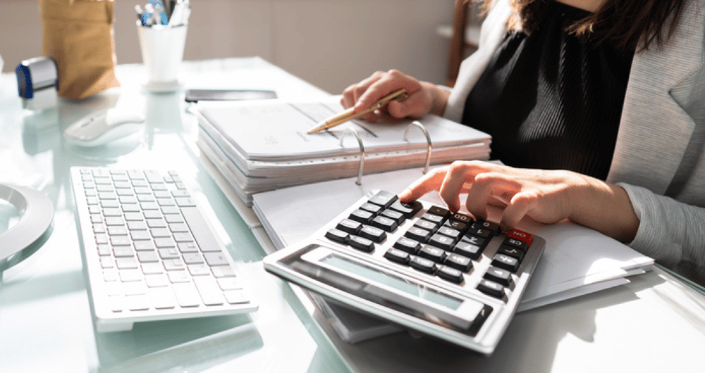 An accounting professional uses a calculator and binder of invoices to figure credits and debits