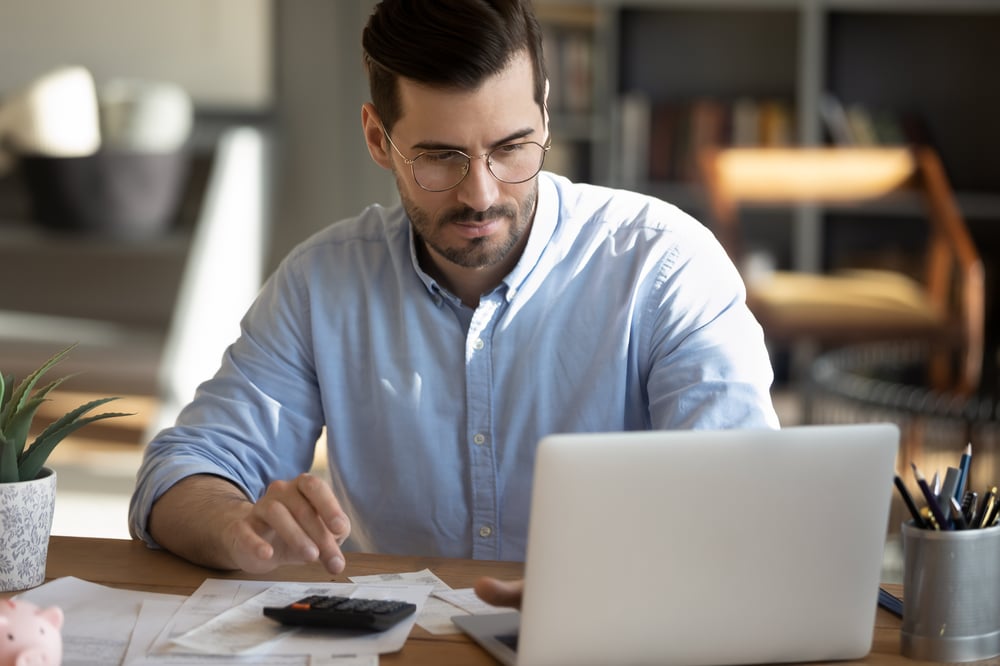 Business professional uses a laptop and calculator to figure out his business’s bookkeeping and accounting